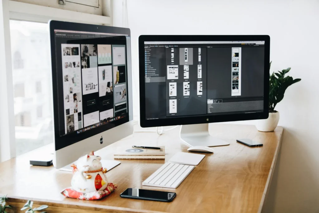 desk with two computer screens showing design items on a dark background